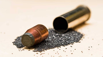 Firearm round split between its casing and projectile sitting atop a gunpowder spill